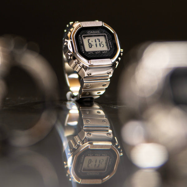 Silver Casio crw001-1 ring watch on a reflective surface with a blurred background