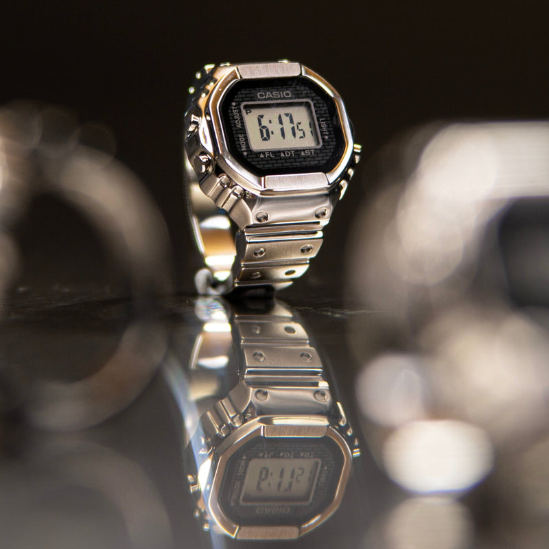 Silver Casio crw001-1 ring watch on a reflective surface with a blurred background